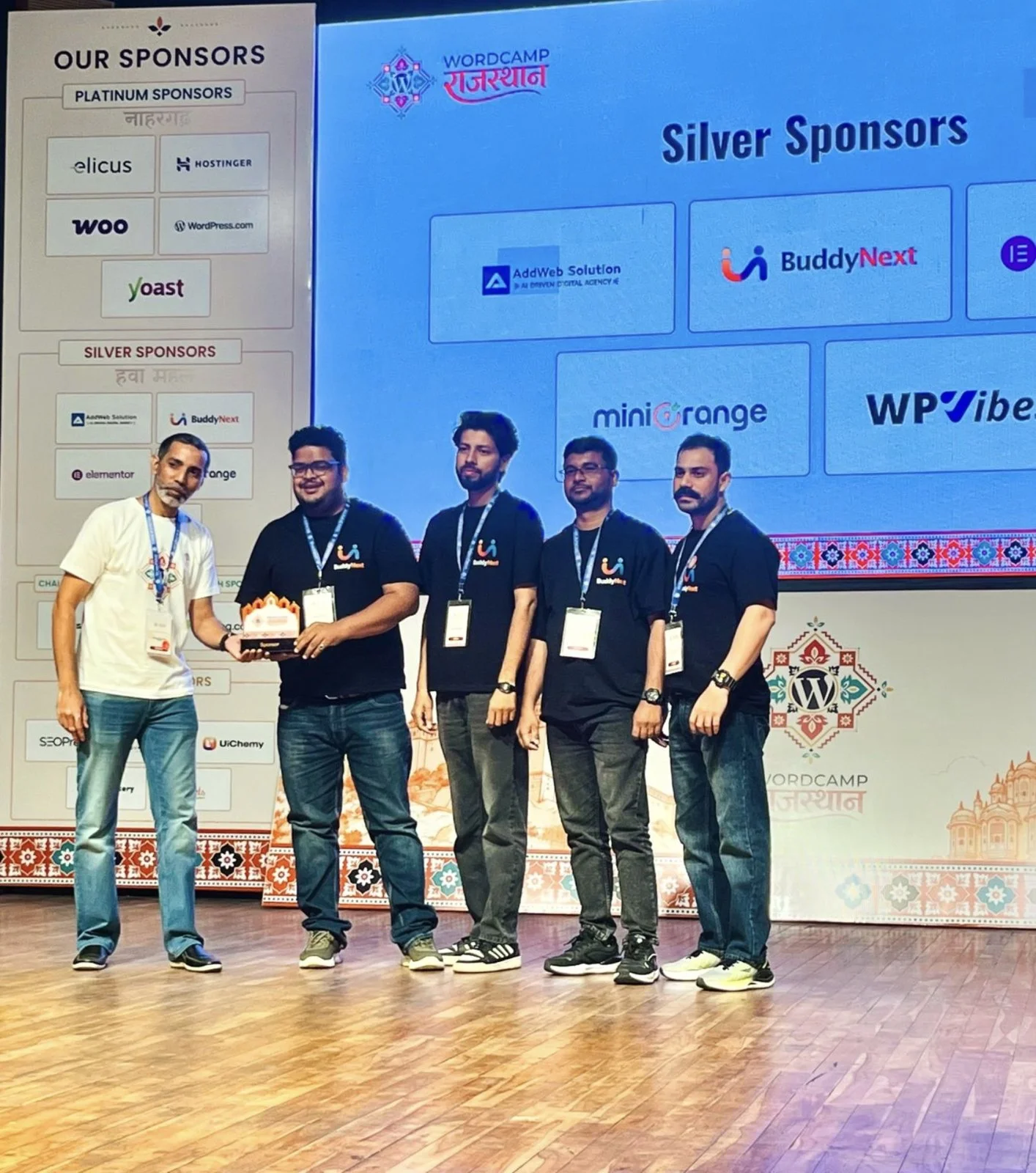 BuddyNext team on stage at WordCamp Rajasthan 2026 receiving the sponsor memento, with the silver sponsors slide behind them