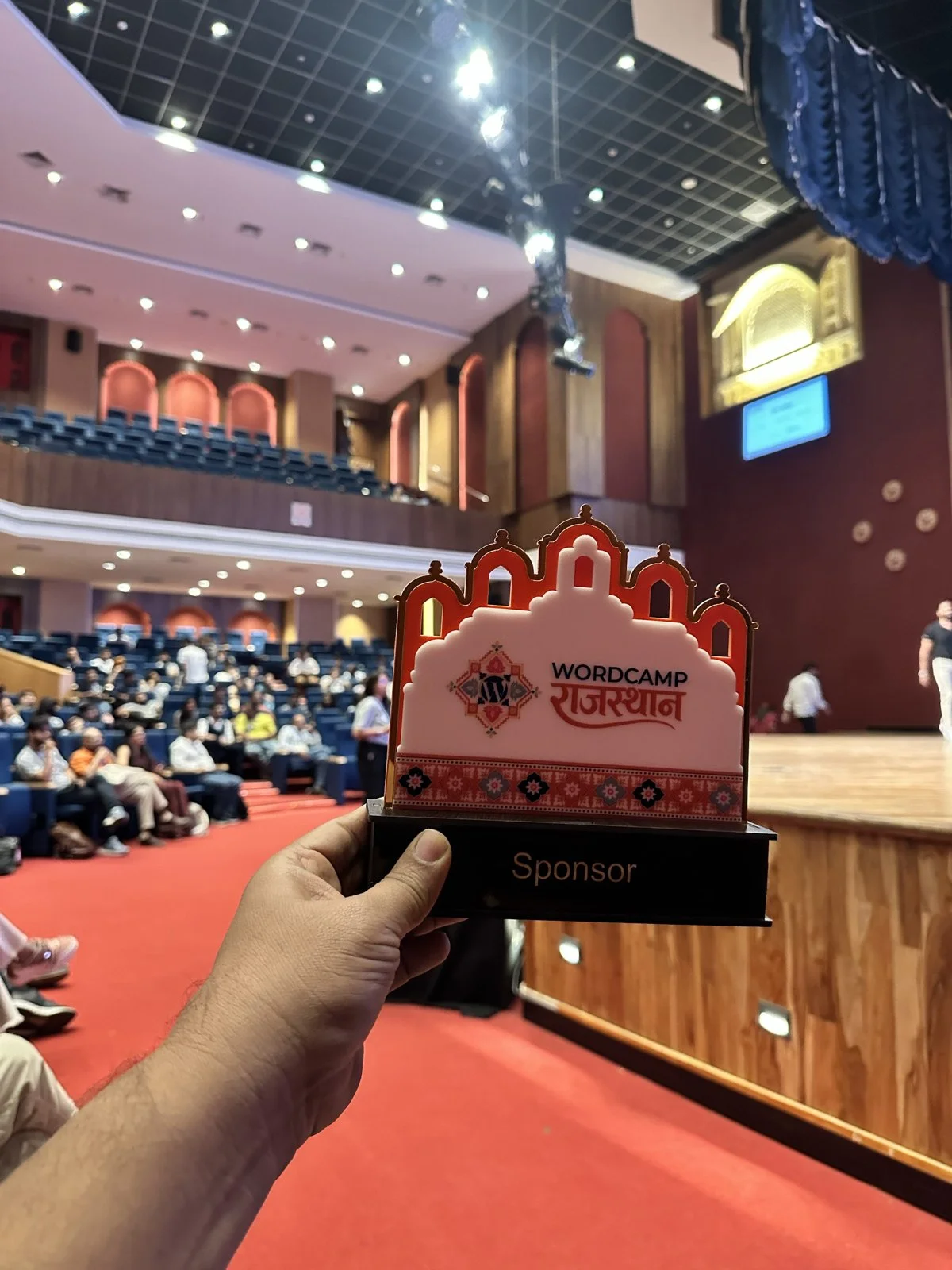 WordCamp Rajasthan 2026 sponsor memento shaped like a Rajasthani palace, held up in the main auditorium